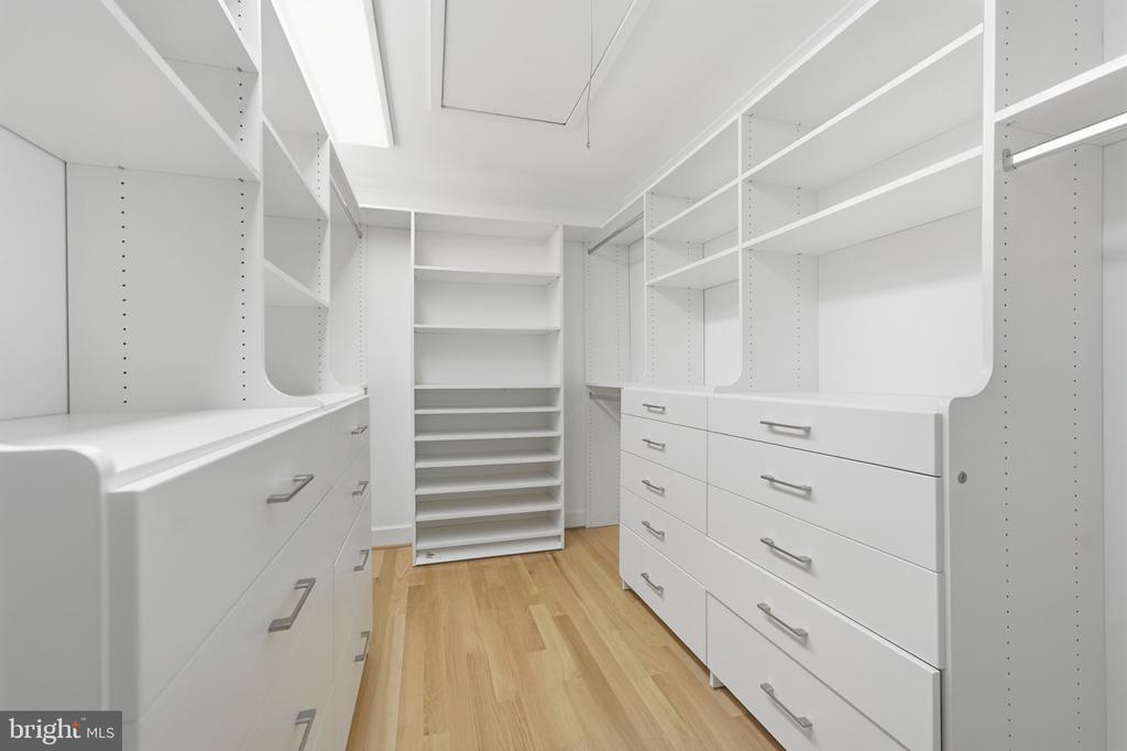 Walk-in closet with white built-in drawers and shelving and light wood flooring.