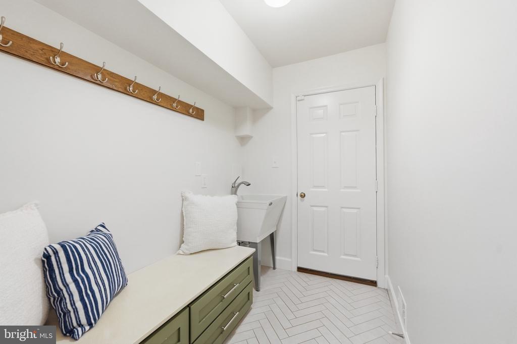 Mudroom with a green built-in bench, wooden coat-hook rack, utility sink, and white herringbone tile floor.