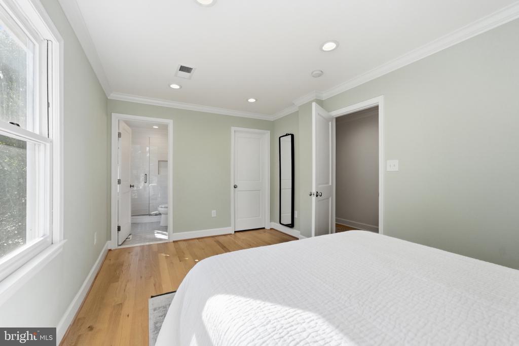 Bedroom with light hardwood floors, a large window, and an adjoining bathroom.