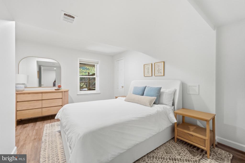 Bedroom with a white bed, blue pillows, light wood furniture, and a patterned rug.