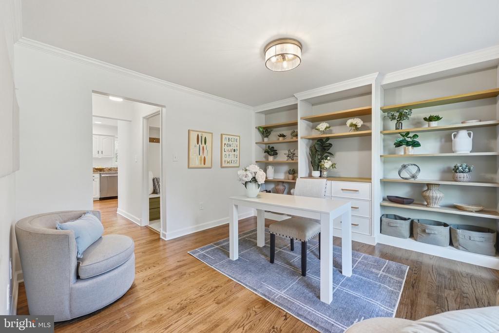 Home office with built-in white shelves, a white table, upholstered chairs, and hardwood floors.