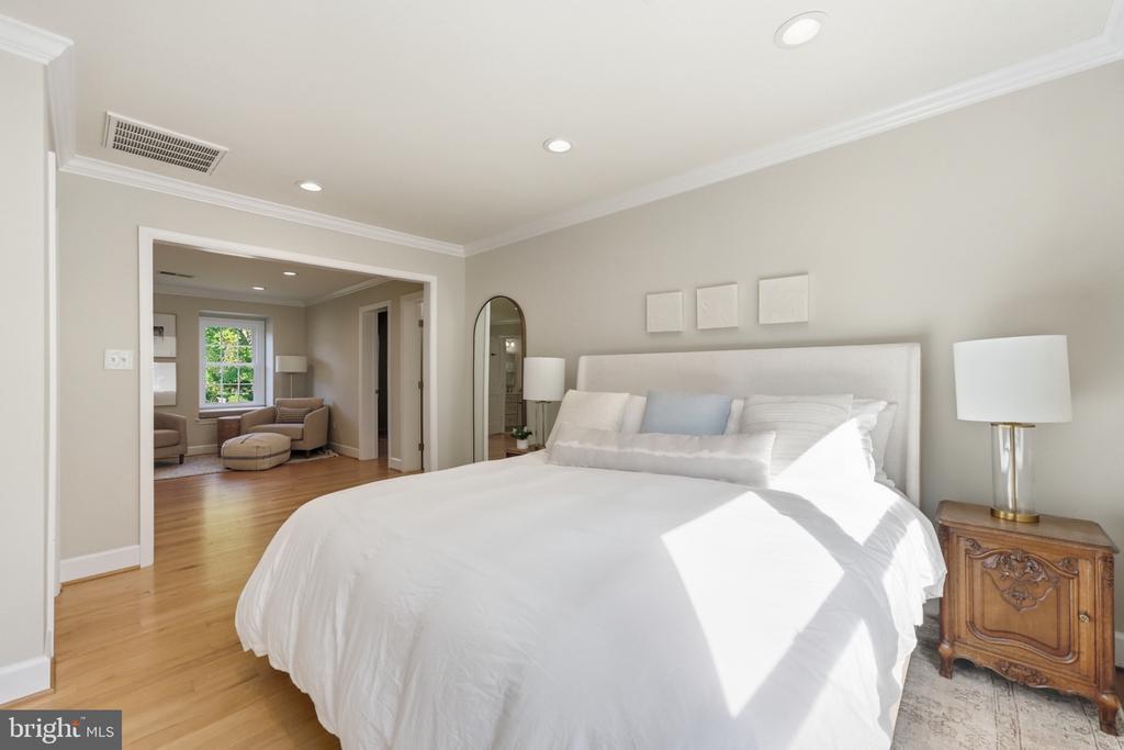 Bedroom with a large white bed and doorway opening to a sitting area with a window.