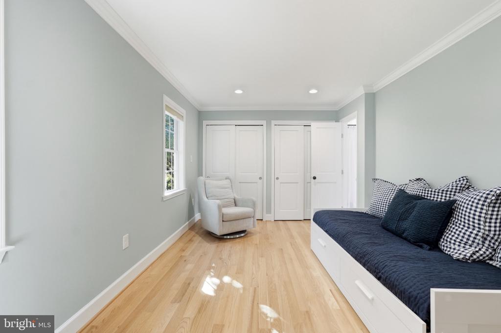 Bedroom with a built-in daybed, hardwood floors, white closet doors, and an upholstered chair.