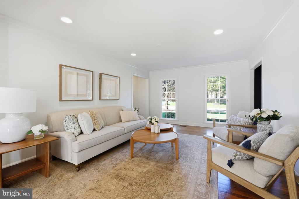 Staged living room with a beige sofa, armchairs, round coffee tables, and two bright windows.