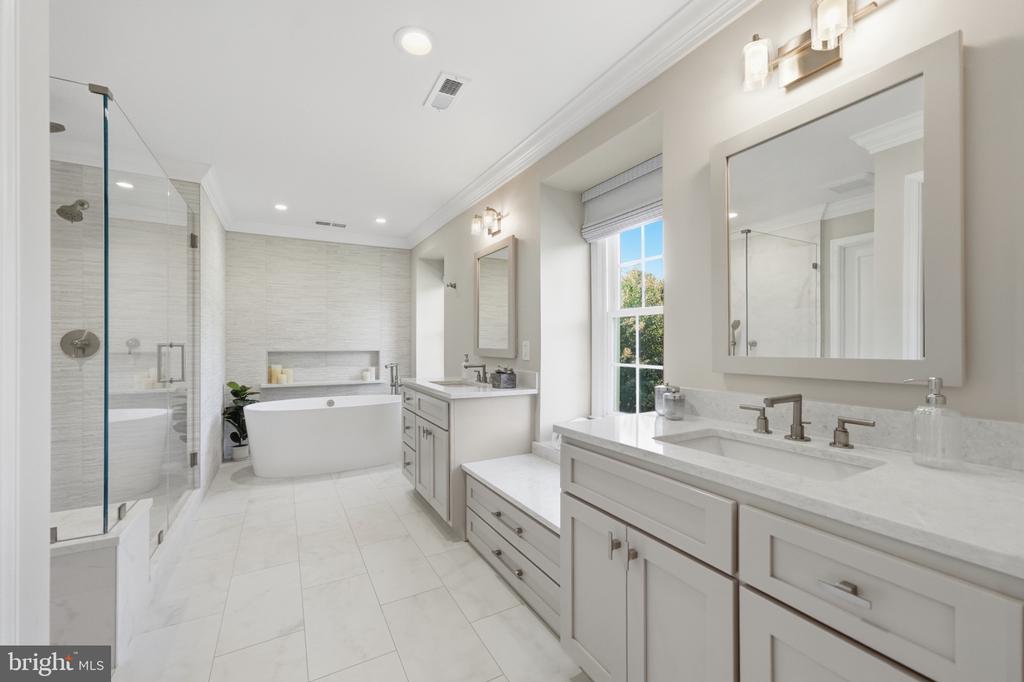 Bright bathroom with a glass shower, freestanding tub, double vanity, and window overlooking trees.