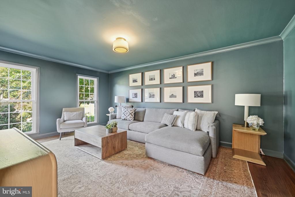 Living room with a gray sectional, blue-gray walls, framed artwork, and large windows.