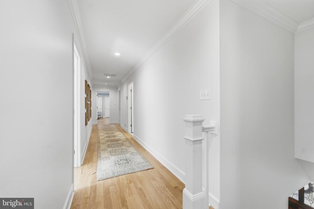 Bright hallway with light wood floors, a patterned runner, and white walls.