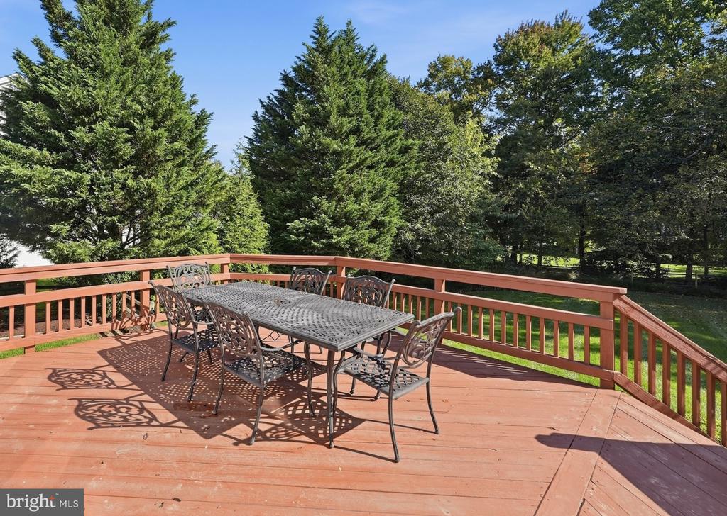 Wood deck with a metal dining set, overlooking a tree-lined lawn.