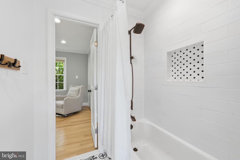 Bathroom with a white subway-tile tub and shower, dotted recessed niche, and an adjoining sitting area.