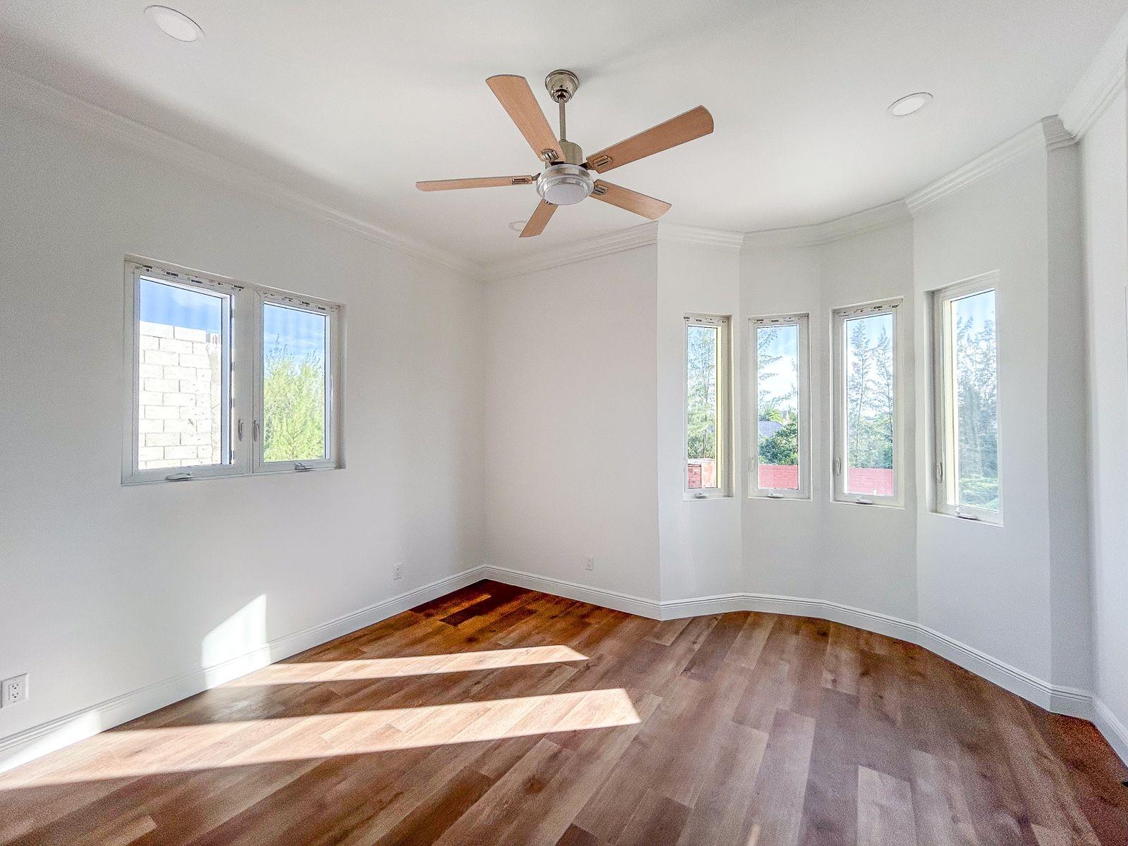 Vacant room with wood floors, a ceiling fan, and a curved bay of windows.