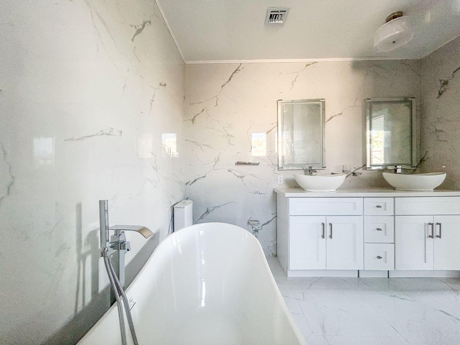 Modern bathroom with a freestanding soaking tub and double vessel-sink vanity against marble-look tile.