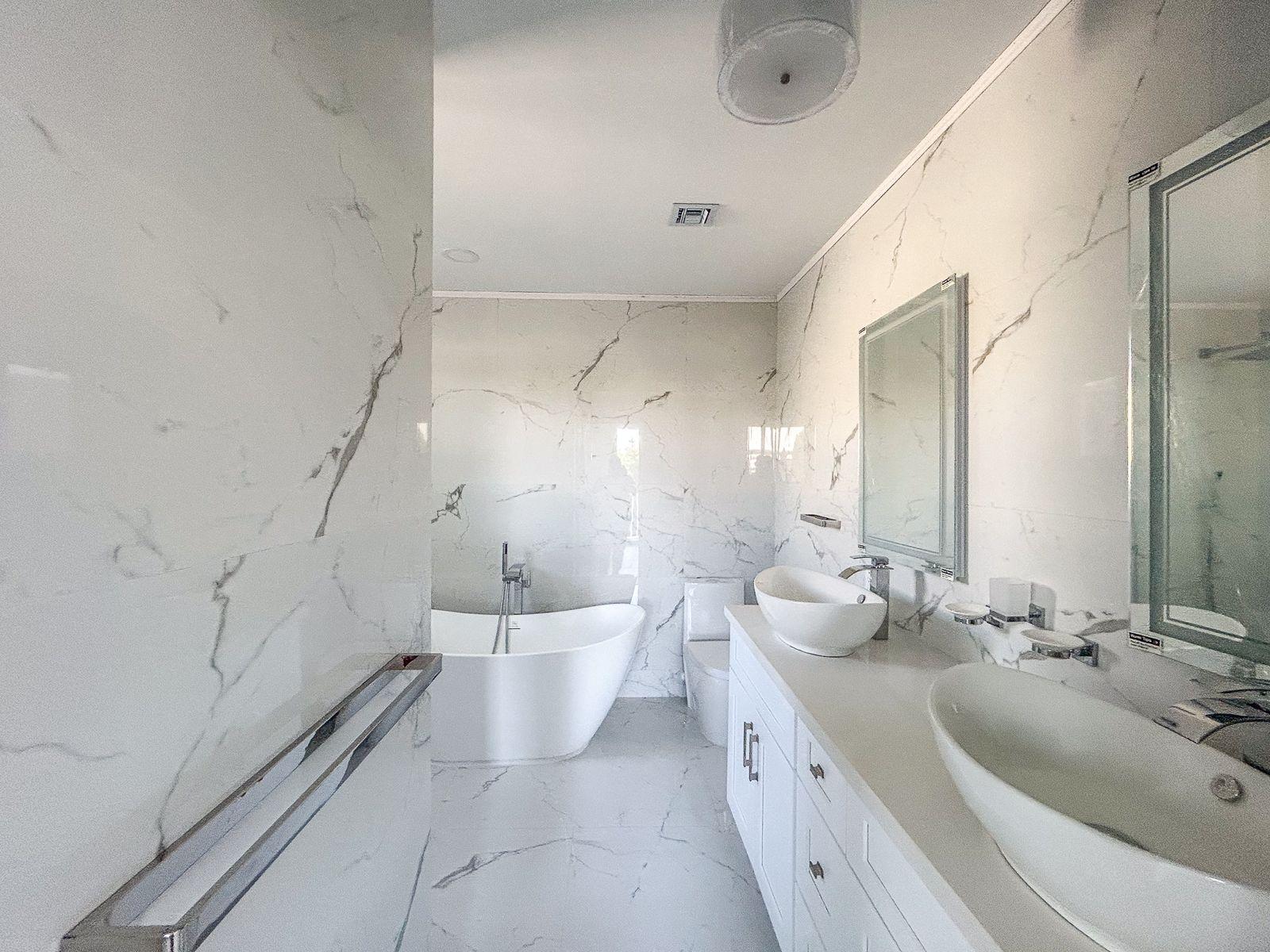 Marble-tiled bathroom with a freestanding soaking tub and double vanity with vessel sinks.