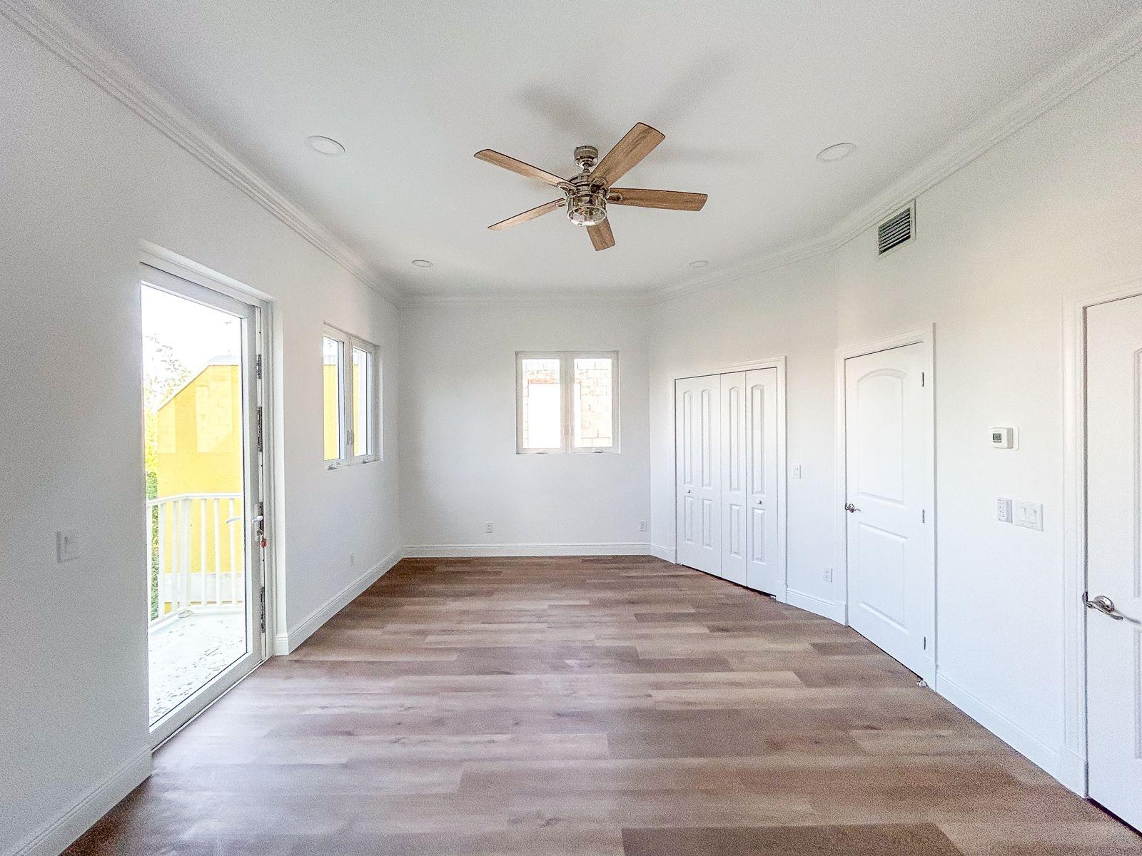 Empty bedroom with wood-look floors, built-in closets, and a glass door to the balcony.