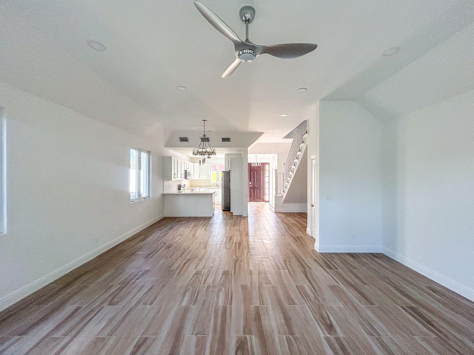 Vacant open-plan living area with wood-look tile floors, white kitchen, and staircase.