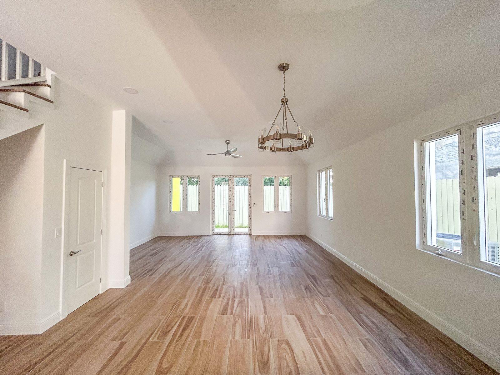 Unfurnished living room with wood floors, a chandelier, and windows overlooking a fenced yard.