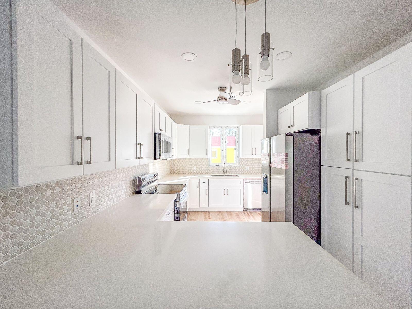 Bright white kitchen with hexagonal tile backsplash, stainless steel appliances, and a broad countertop.