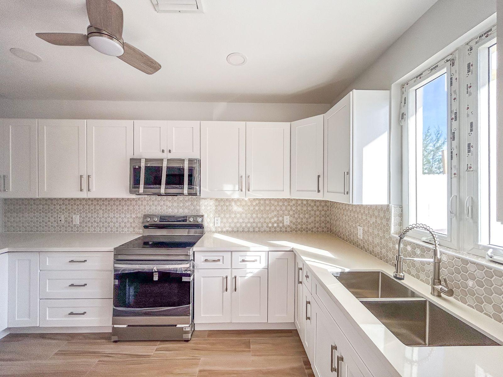 Bright kitchen with white cabinets, hexagonal tile backsplash, stainless steel range, and double-basin sink by tall windows.