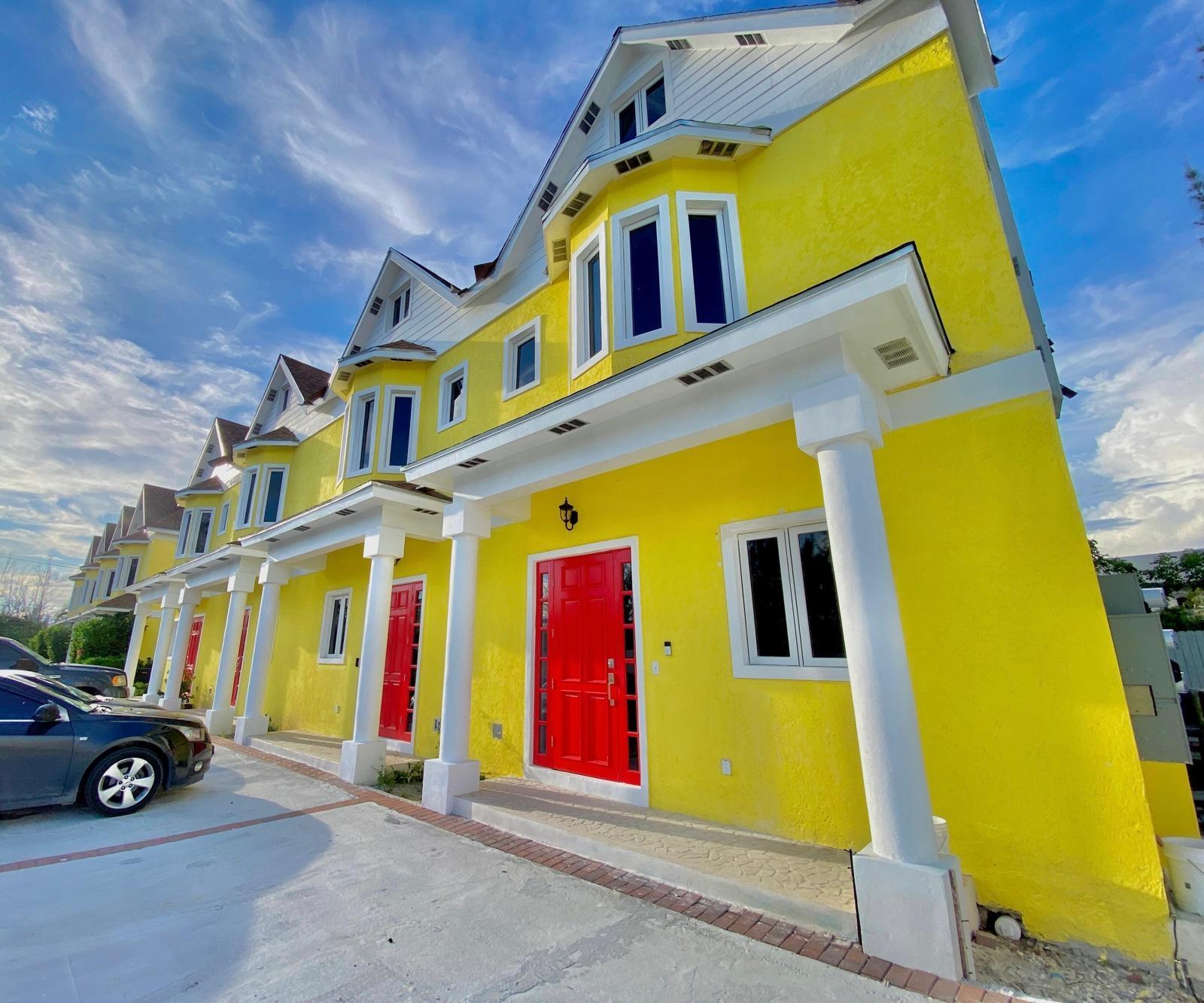 Yellow attached homes with white trim and columns, red front doors, and a paved parking area.