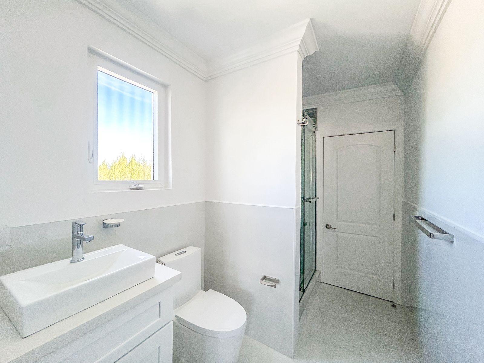 Bright bathroom with a vessel sink, toilet, glass shower, and window.