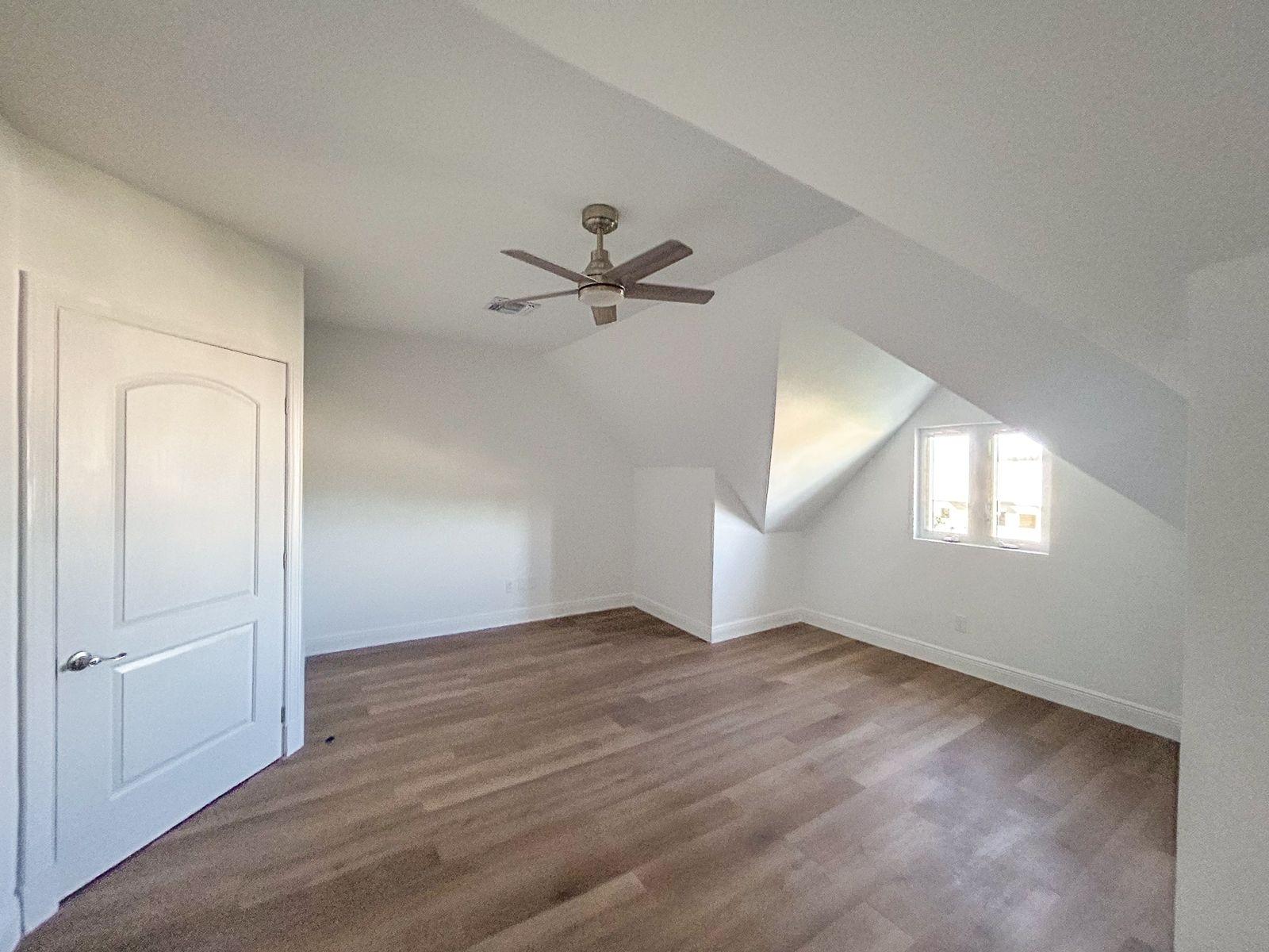 Empty bedroom with sloped ceilings, wood-look flooring, and a ceiling fan.