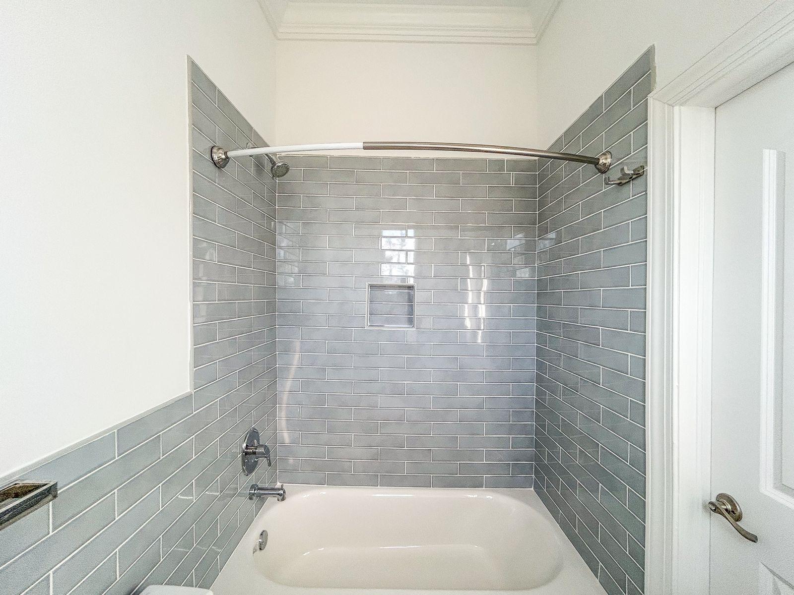 Bathroom with a white bathtub, gray subway tile, and a chrome shower rod.