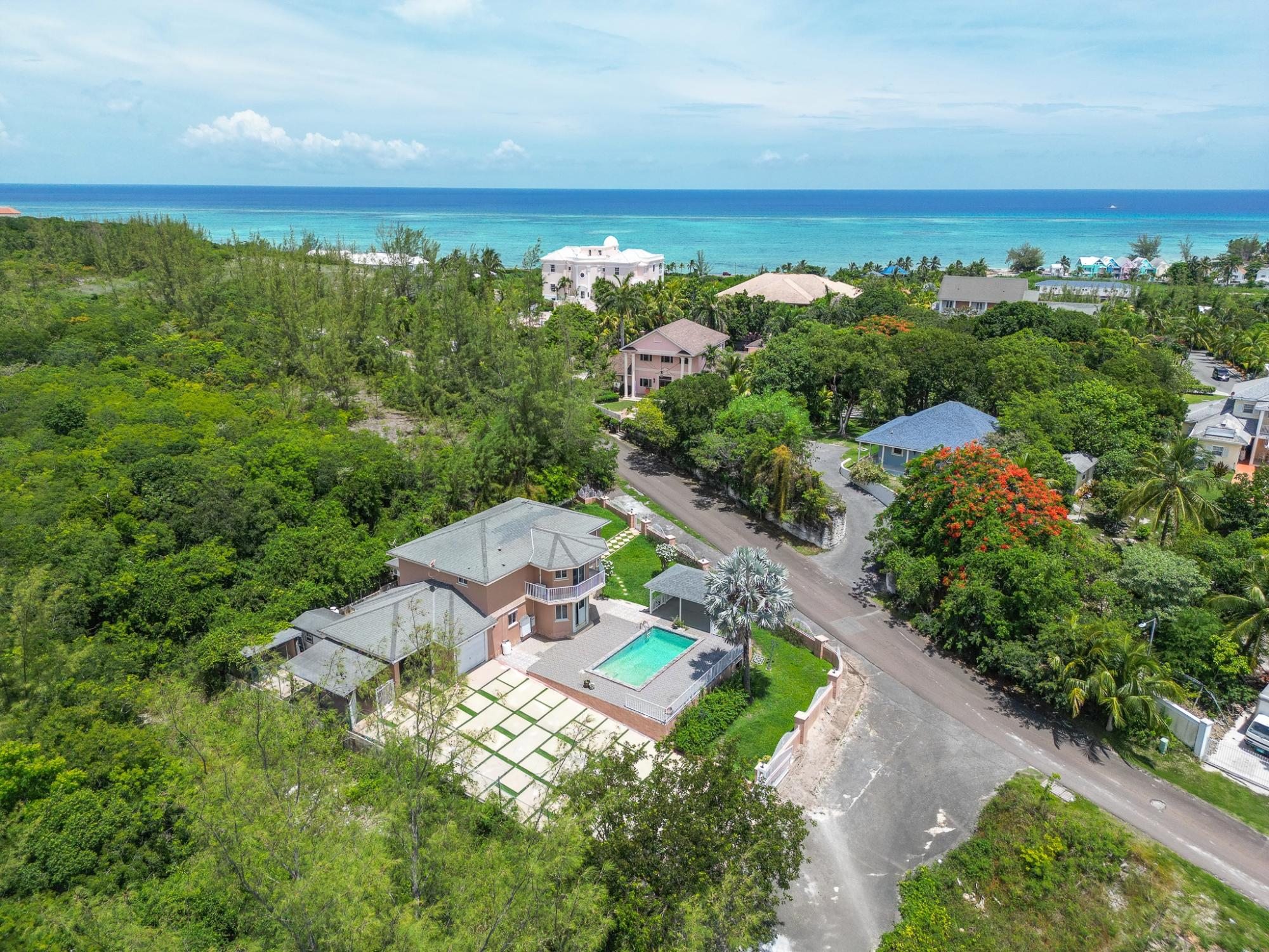 Aerial view of a two-story home with a turquoise pool, surrounded by tropical greenery near the ocean.