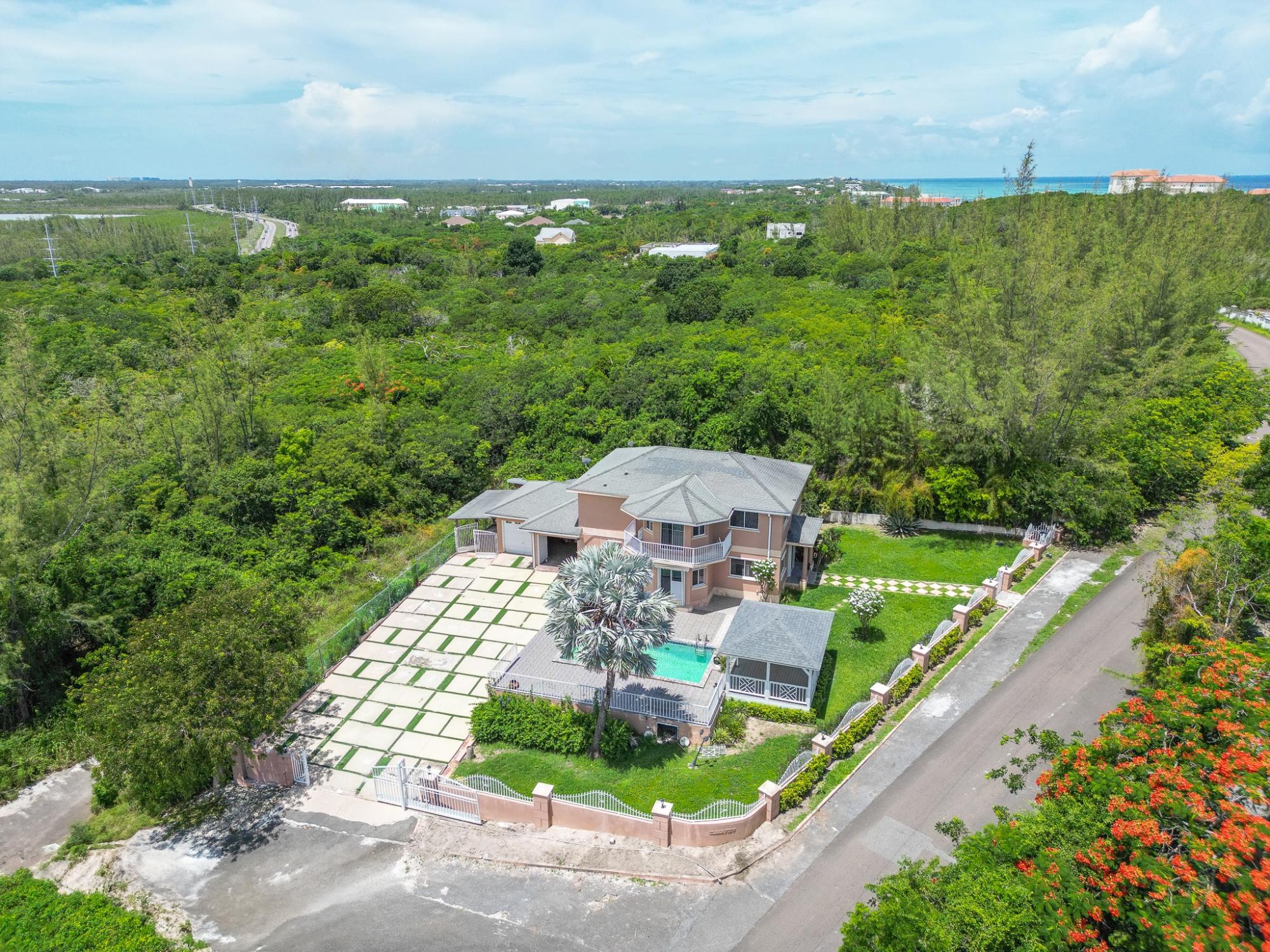 Aerial view of a two-story home with a pool, expansive paved driveway, and ocean in the distance.
