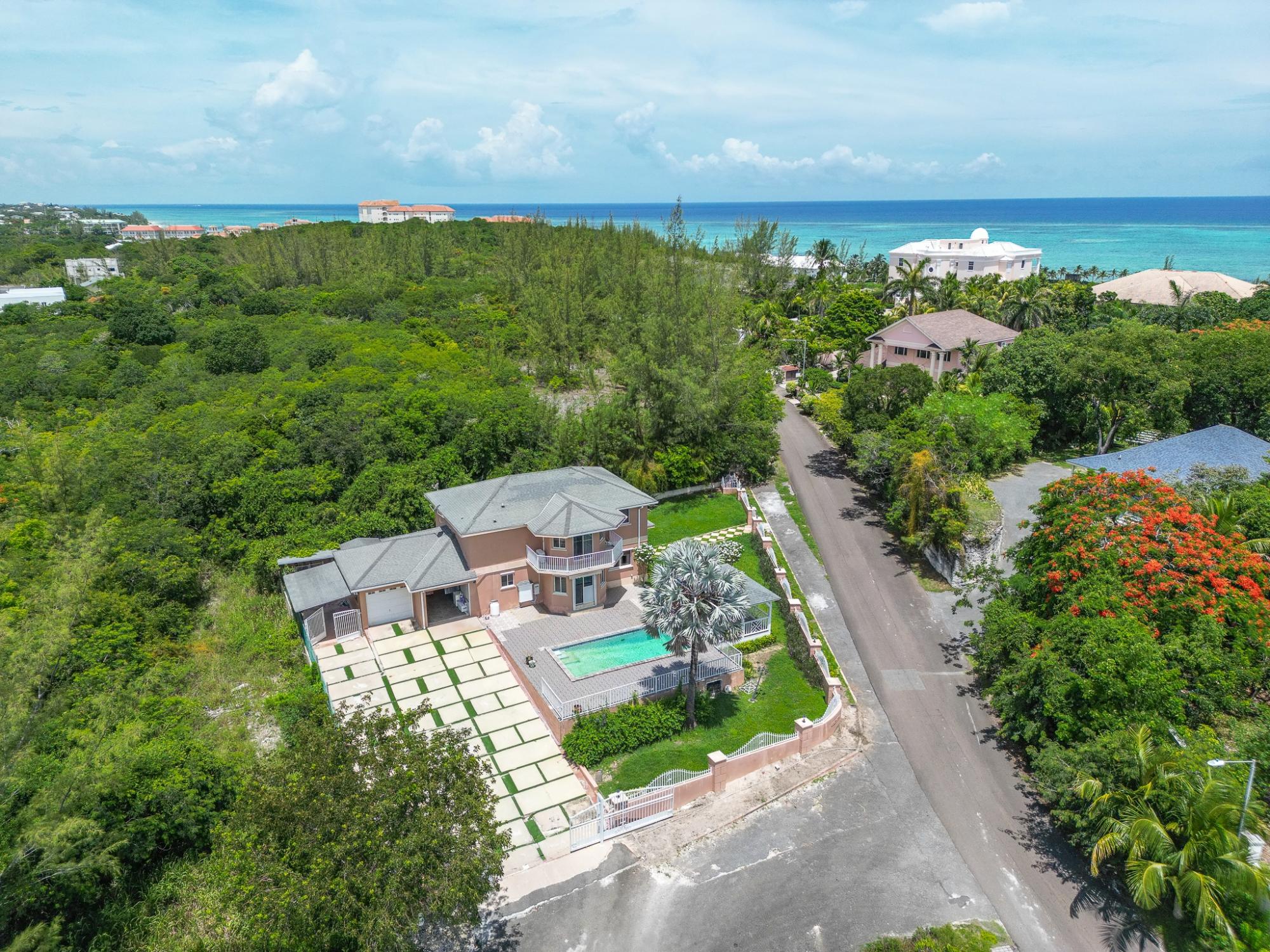 Aerial view of a coastal home with a swimming pool, tropical greenery, and ocean beyond.