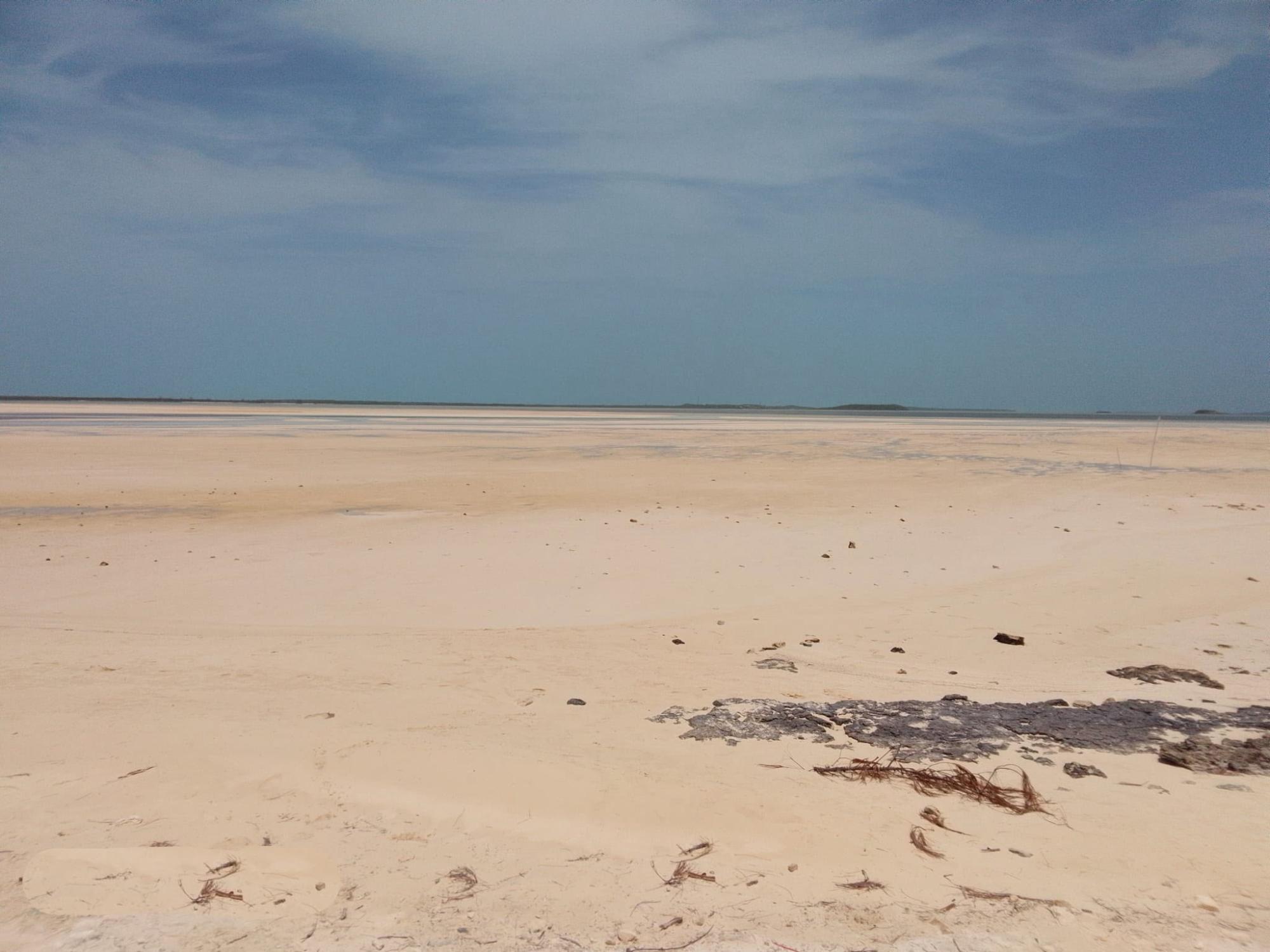 Pale sandy beach and tidal flats stretch toward calm water and low islands on the horizon.