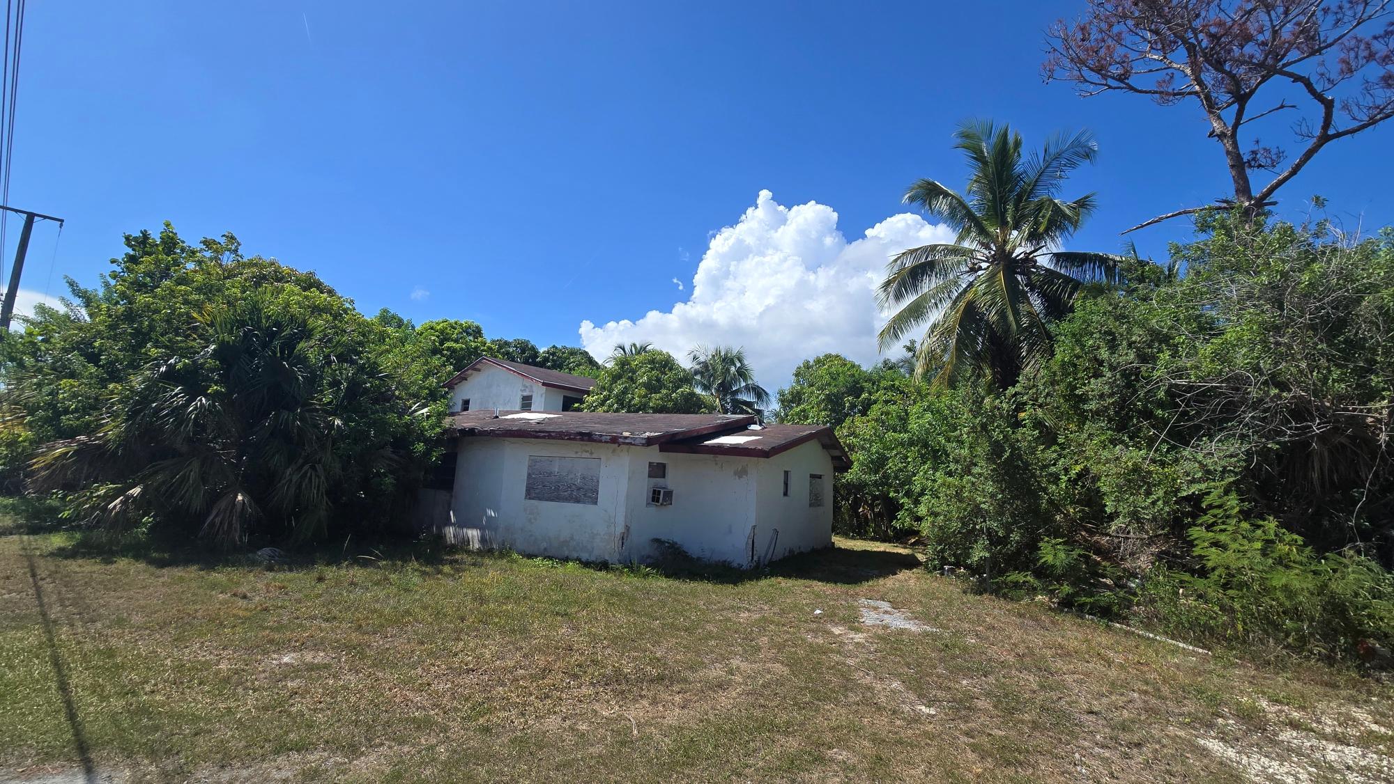 White house with weathered walls and reddish-brown roofs amid dense tropical greenery.