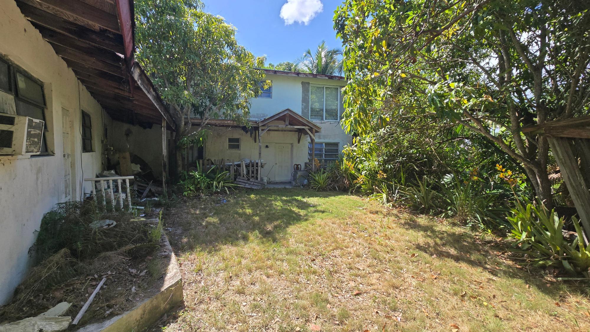 Weathered two-story house behind a grassy yard, surrounded by dense tropical trees and plants.