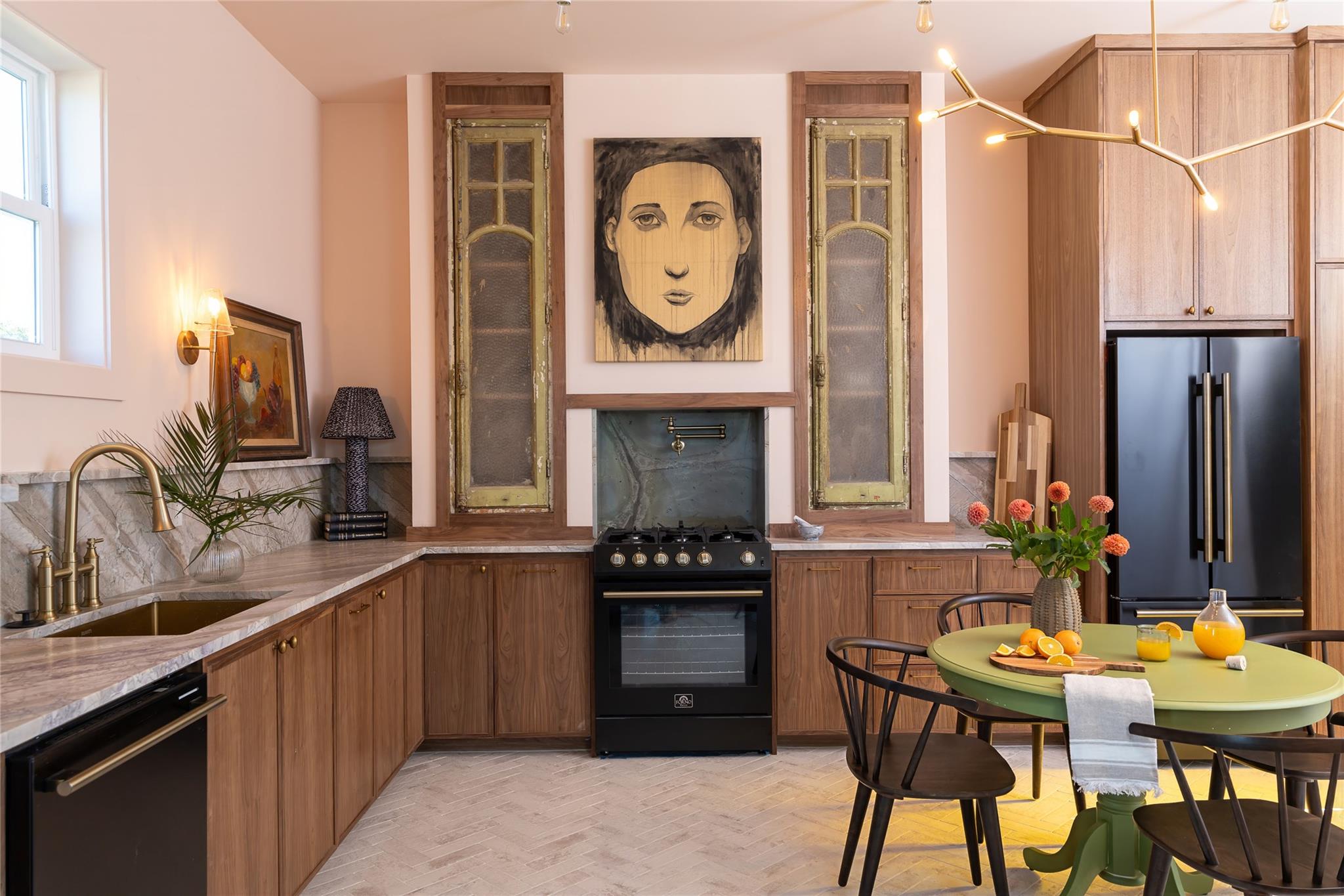 Kitchen with walnut cabinets, marble counters, black range, and a green dining table beneath portrait artwork.