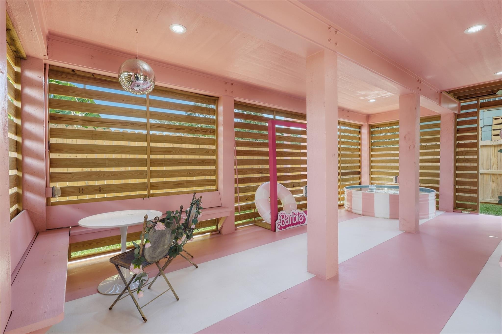 Pink covered patio with a striped soaking pool, wooden slat screens, and Barbie-themed decor.