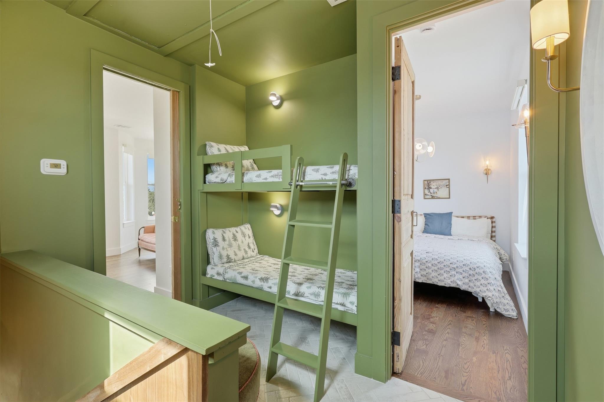 Green bunk room with built-in twin beds and ladder beside a doorway to a bedroom.