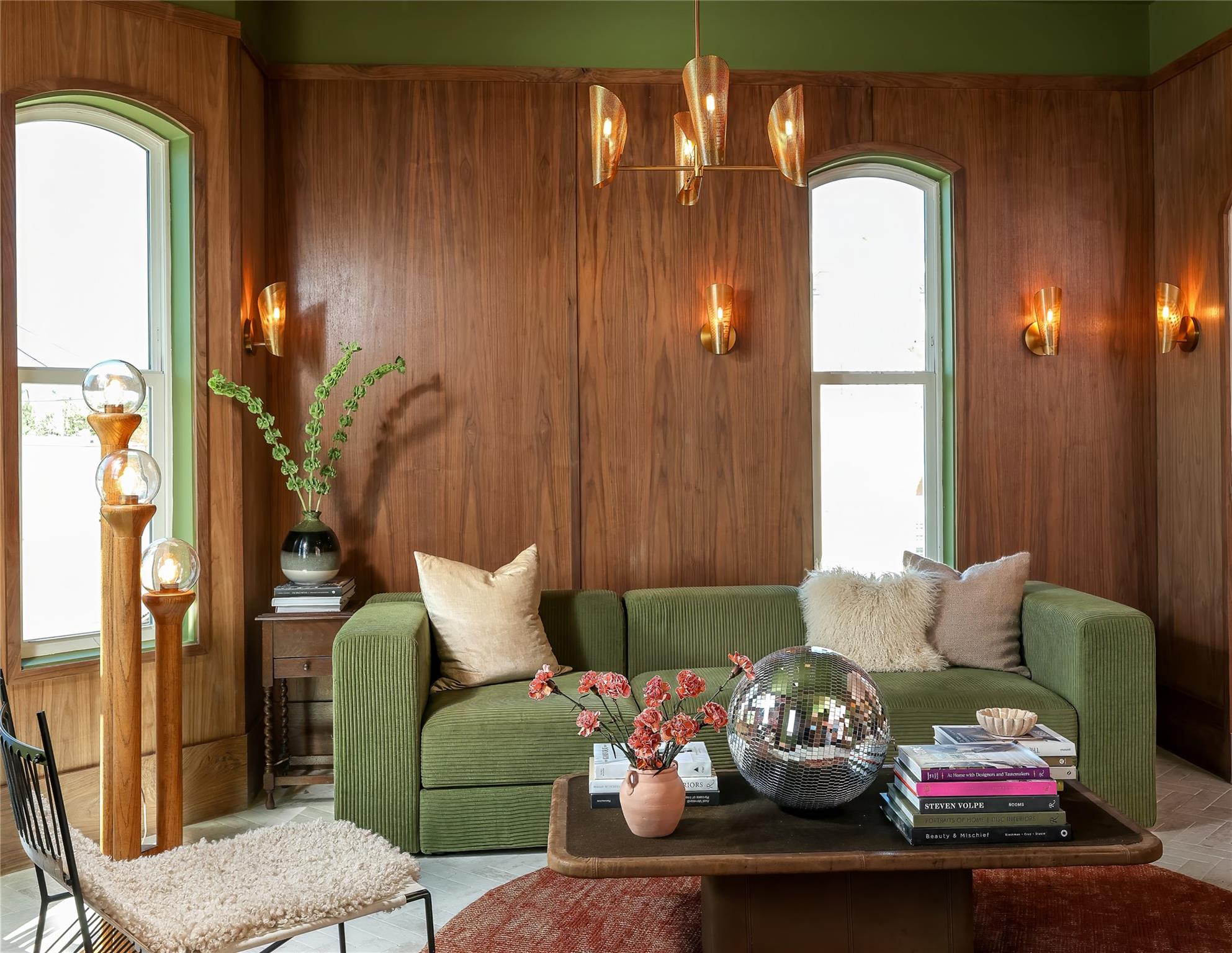 Living room with a green sofa against walnut-paneled walls and tall arched windows.