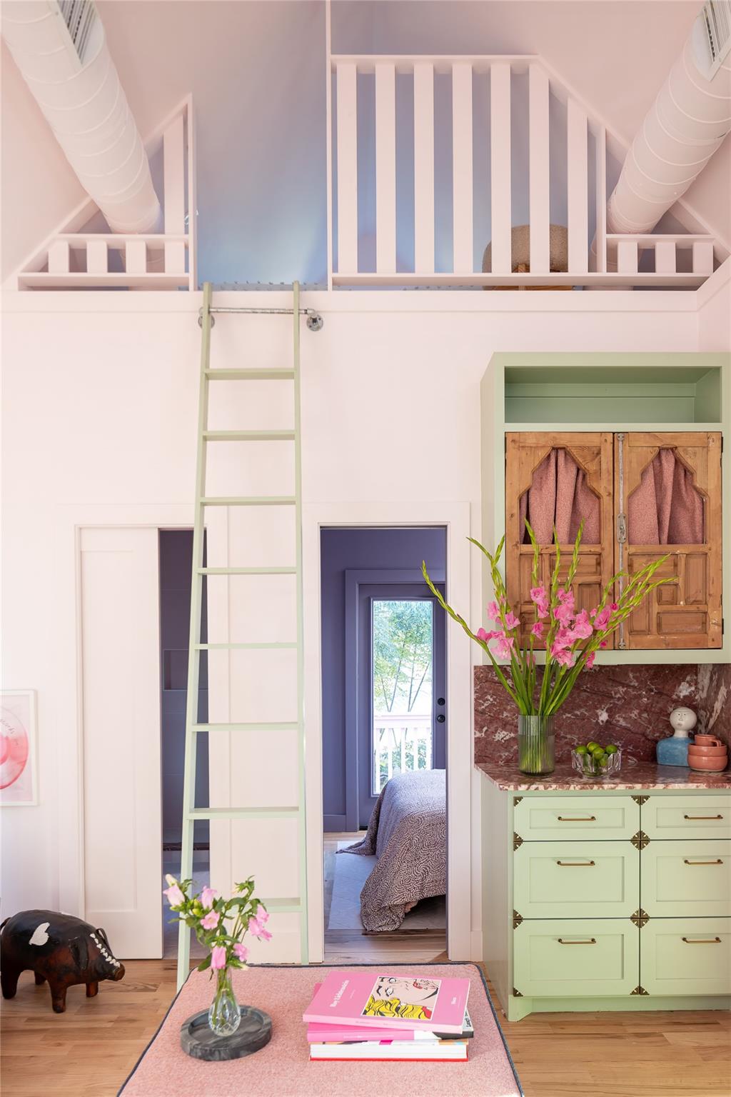 Bright interior with a ladder to a loft, mint-green cabinetry, and a bedroom visible through the doorway.