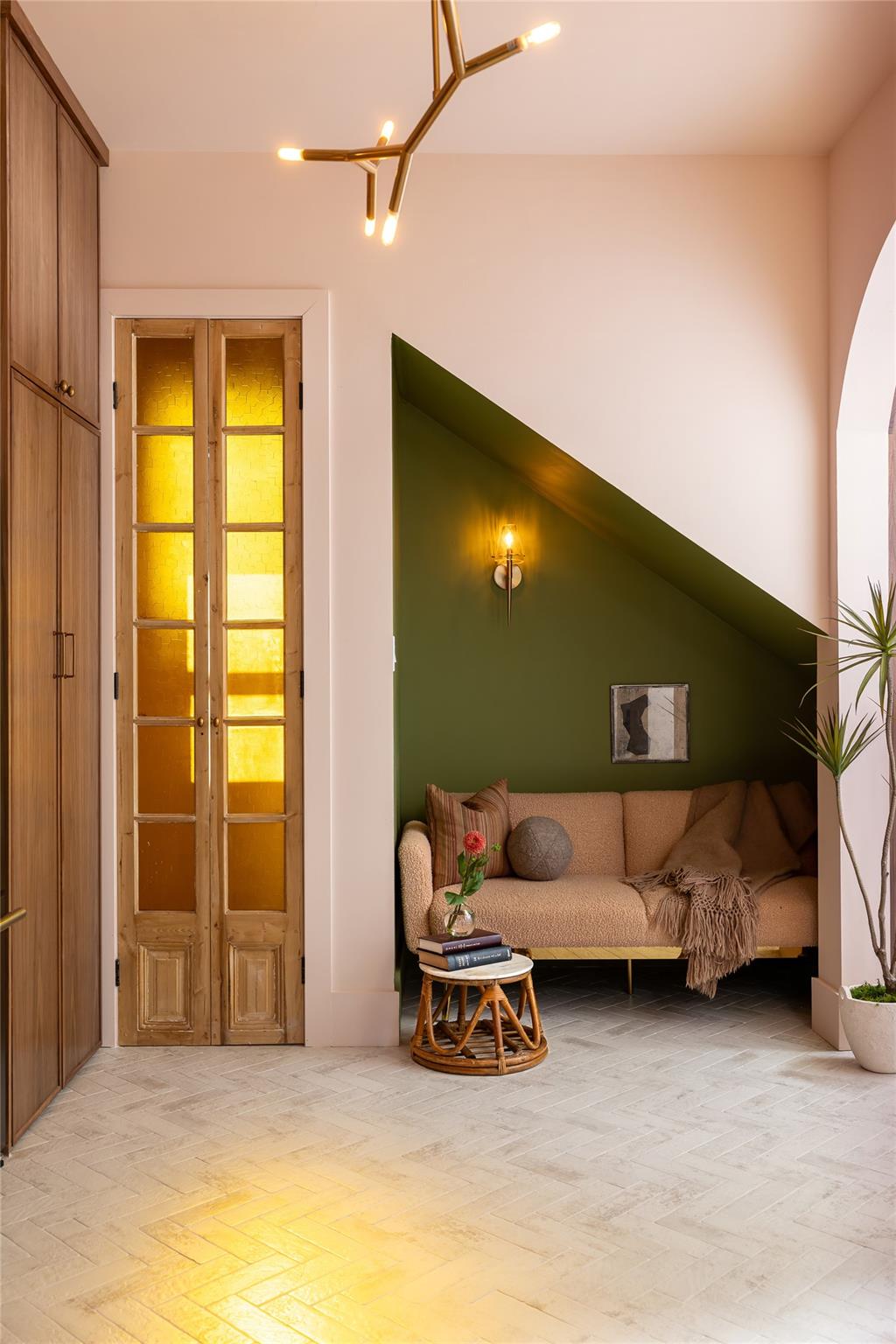 Living room nook with a blush sofa beneath a dark green sloped wall and amber-glass French doors.
