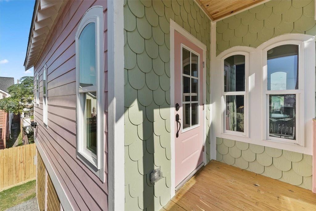 Covered porch with a pink door, arched windows, scalloped green shingles, and a wood deck.