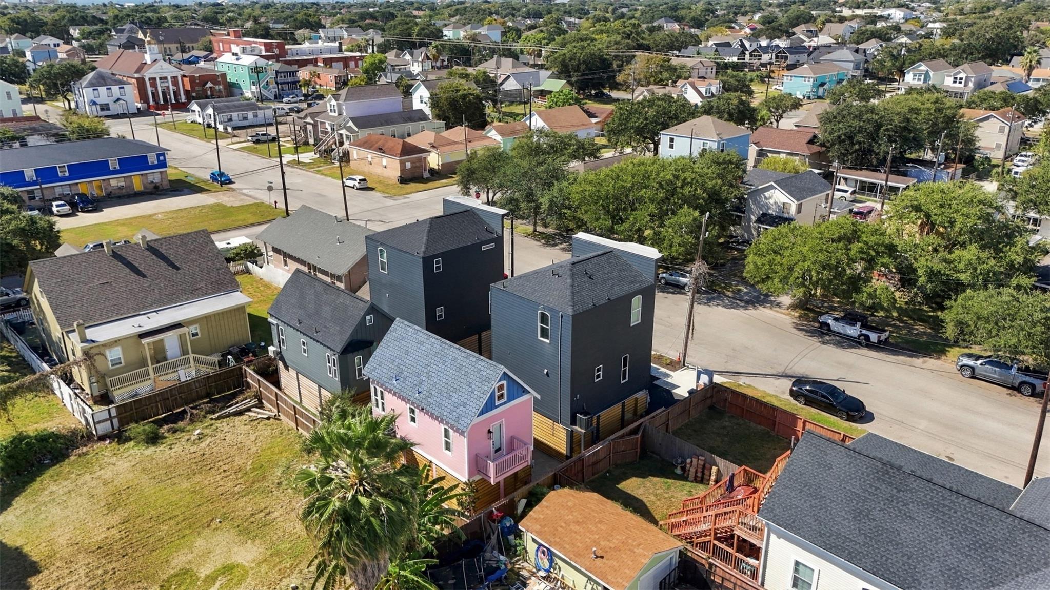 Aerial view of a Galveston neighborhood with colorful homes, fenced yards, and tree-lined streets.