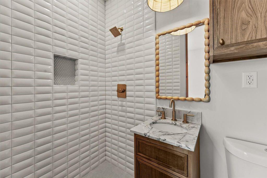 Bathroom with a white tiled shower, marble vanity, and wood cabinet.