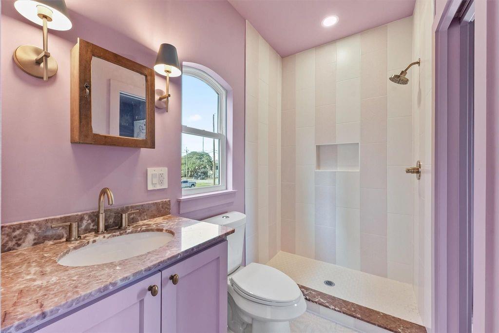 Bathroom with lavender vanity and walls, arched window, and white tiled walk-in shower.