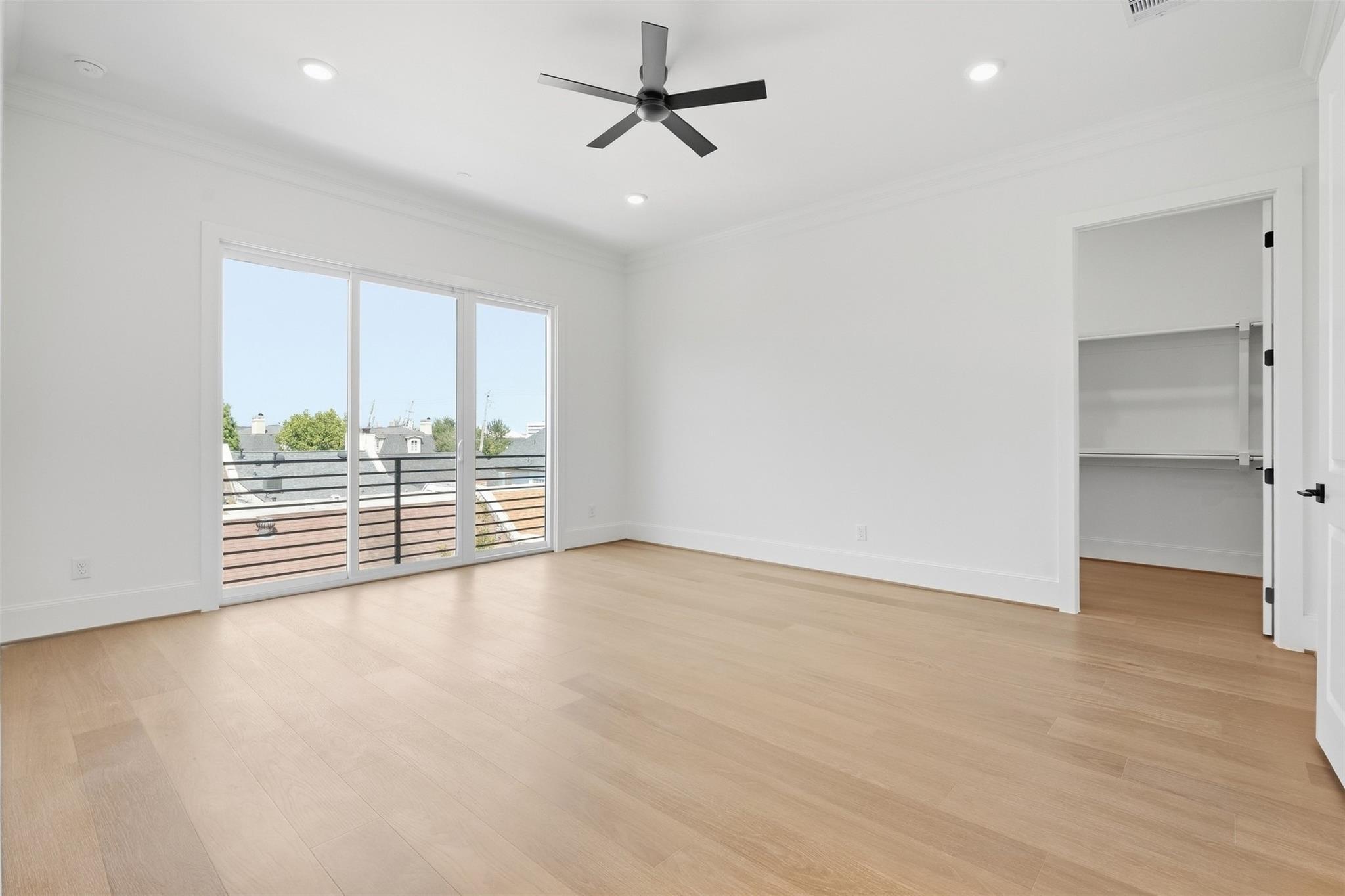 Vacant bedroom with pale wood floors, a black ceiling fan, and sliding glass doors to a balcony.