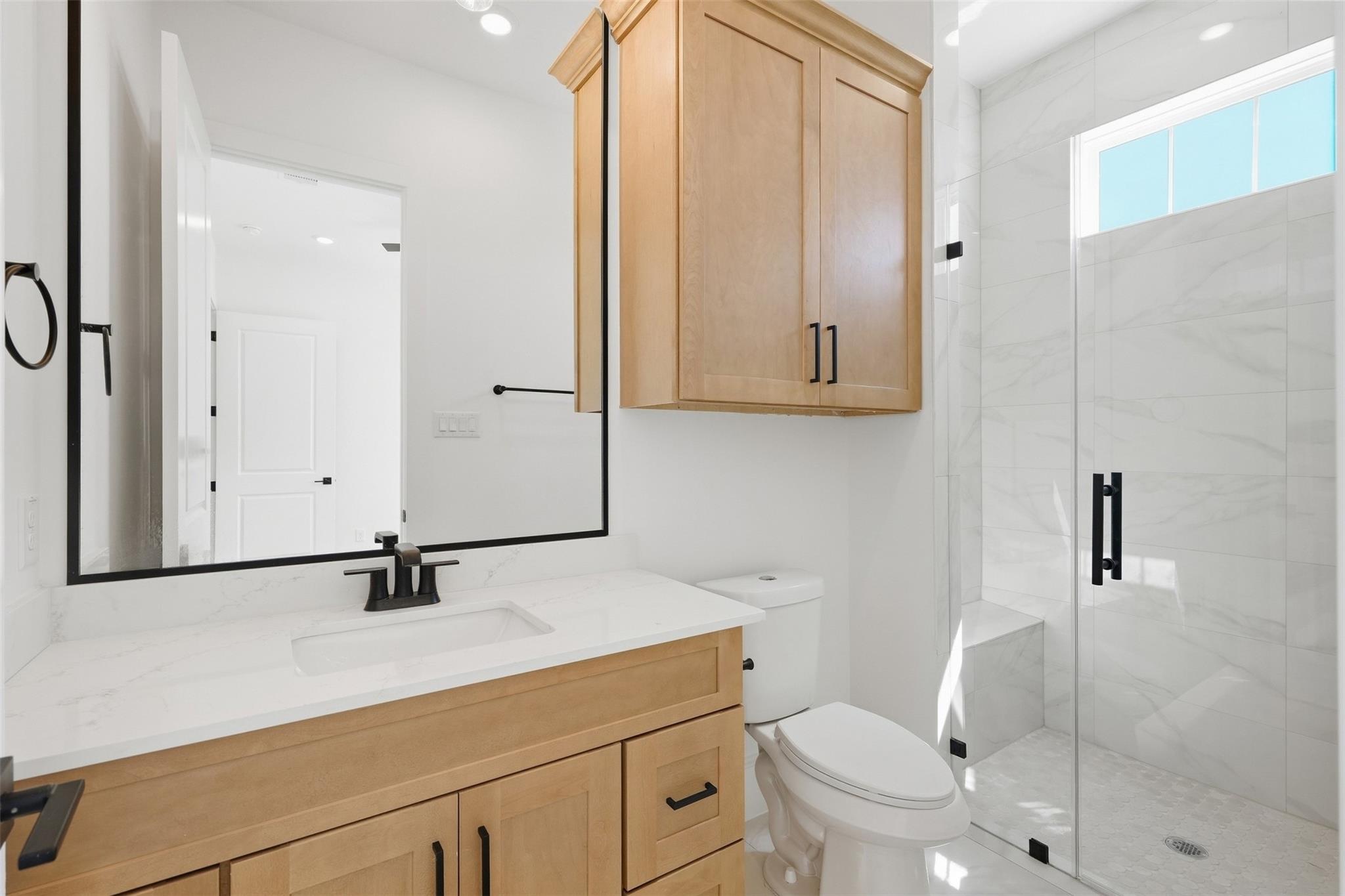 Modern bathroom with light wood cabinetry, a white vanity, and a glass-enclosed tiled shower.