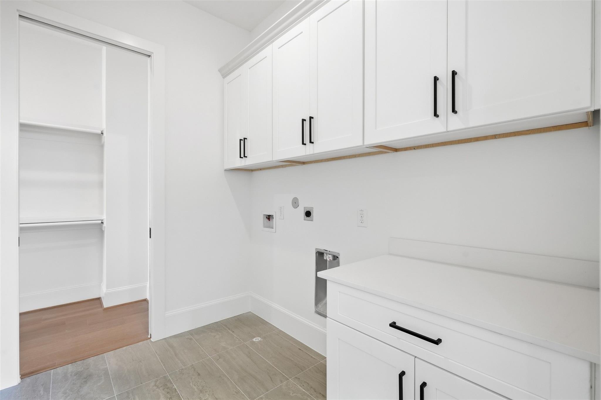 Laundry room with white cabinets, a folding counter, washer hookups, and a built-in shelving closet.