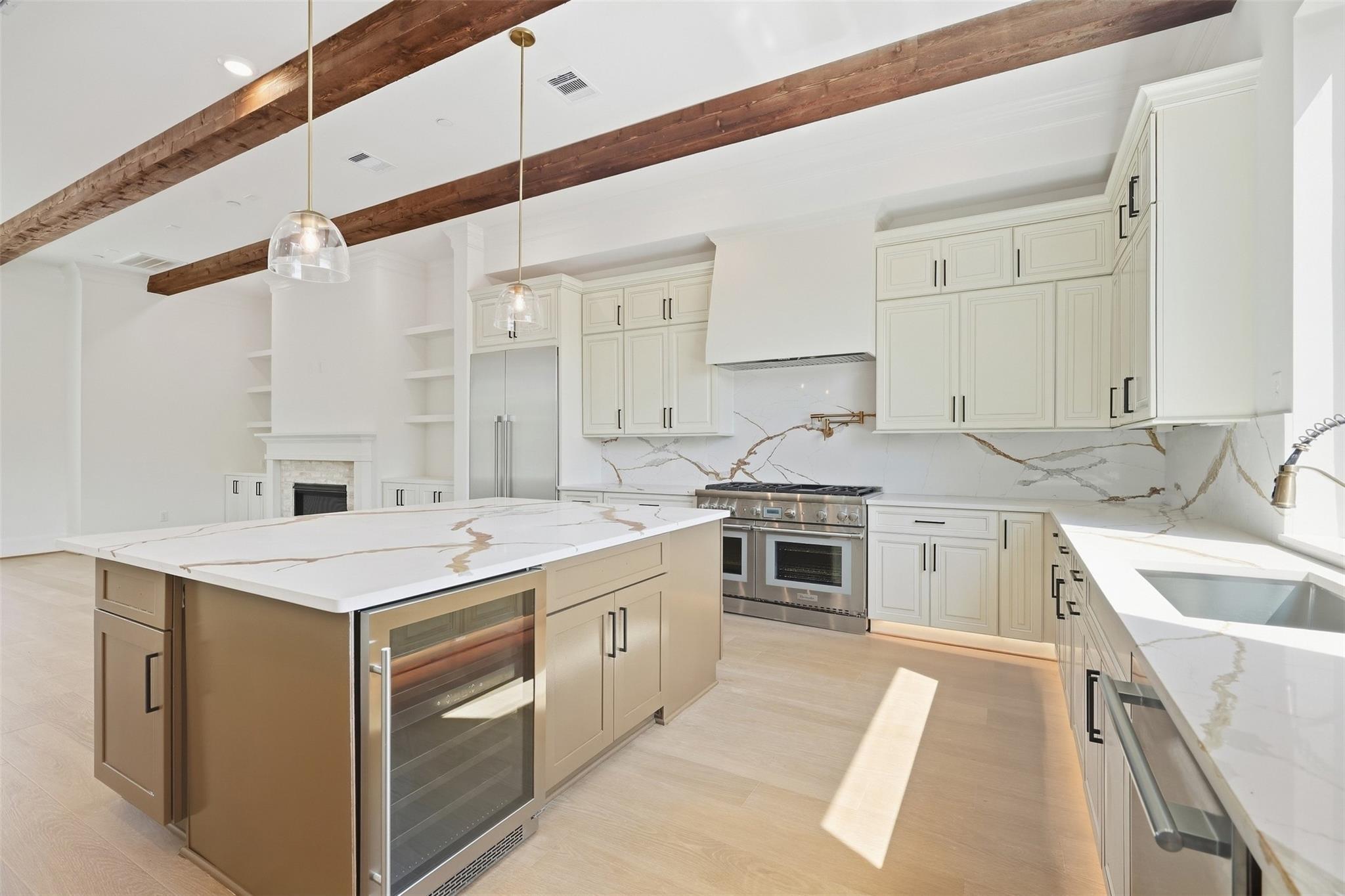 Kitchen with a marble island, white cabinetry, stainless appliances, and exposed wood ceiling beams.