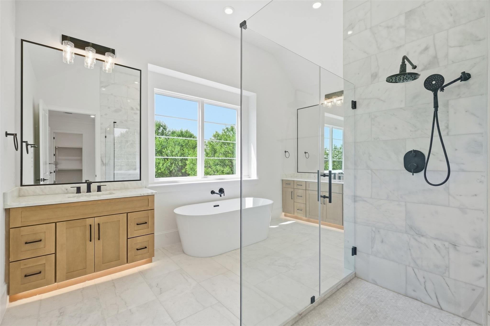 Bright marble bathroom with a freestanding tub, wood vanity, and glass walk-in shower.