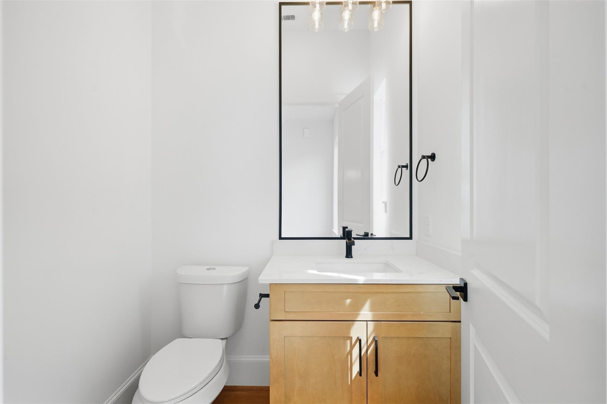 Bathroom with a light wood vanity, black fixtures, and a toilet beside the sink.