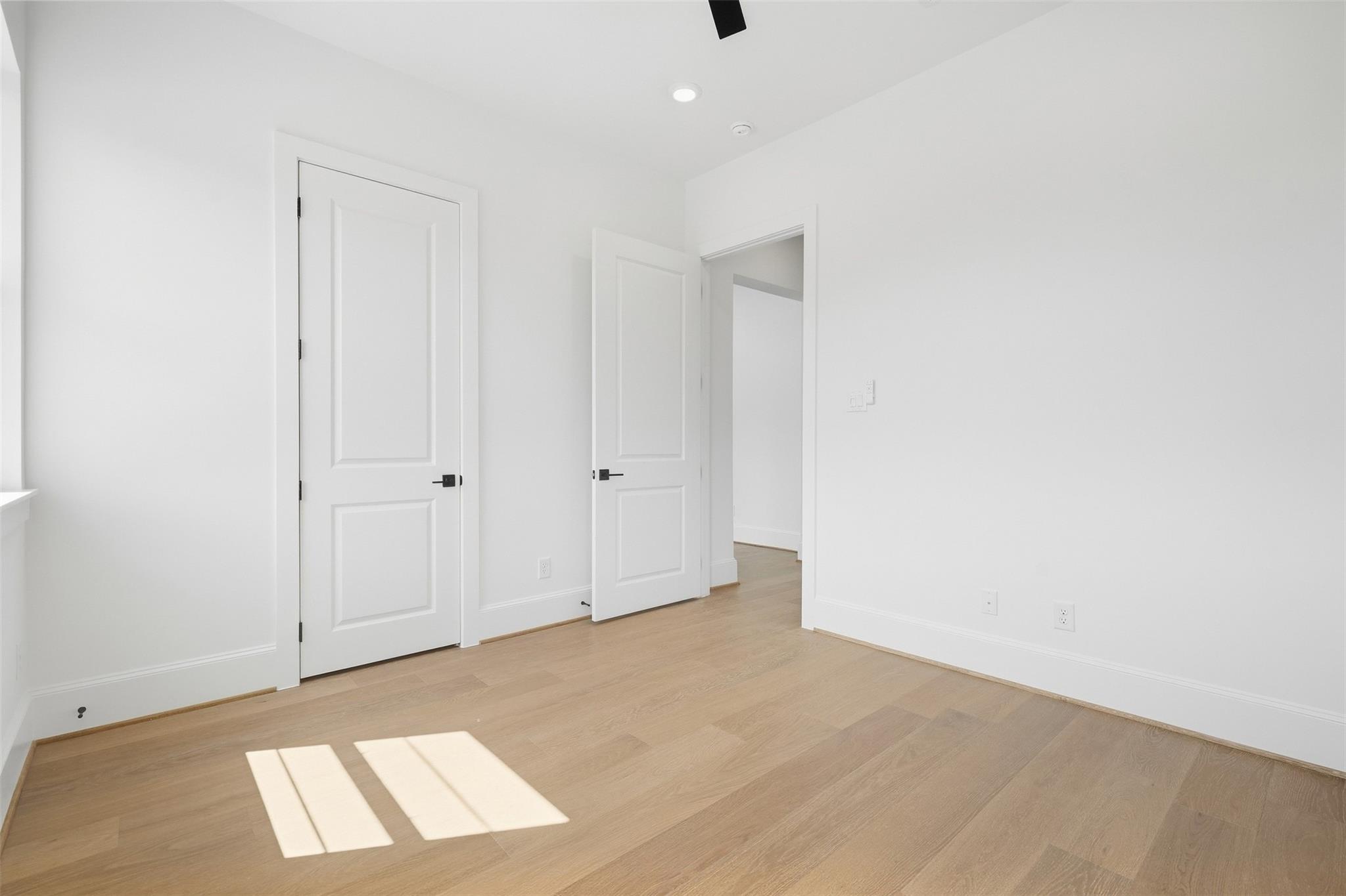 Empty room with light wood floors, white paneled doors, and sunlight across the floor.