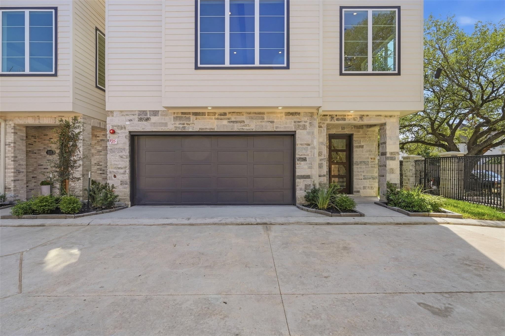 Townhouse exterior with a stone facade, dark garage door, landscaped entry, and broad driveway.
