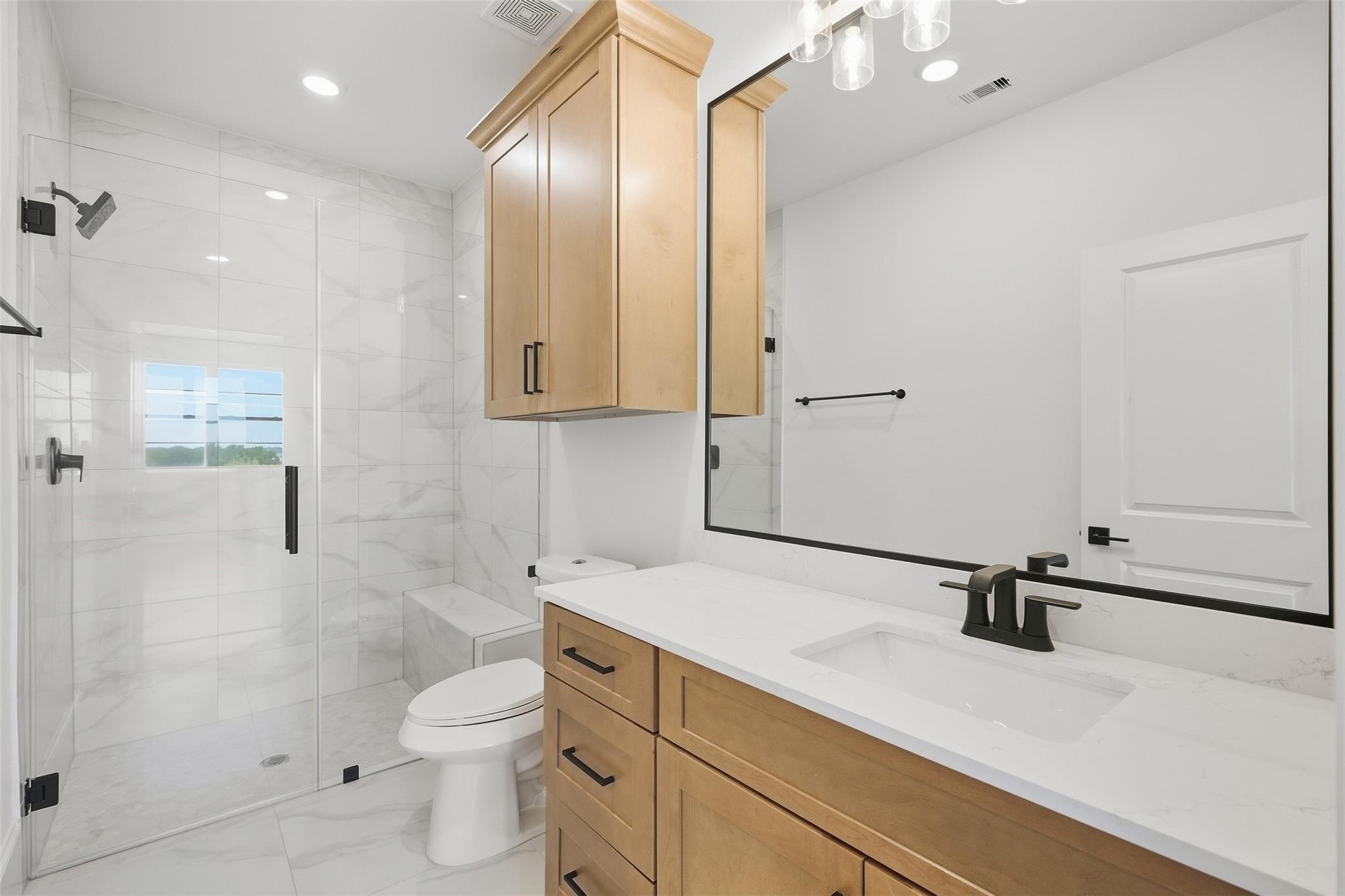 Modern bathroom with a glass shower, wood vanity, white tile, and black fixtures.